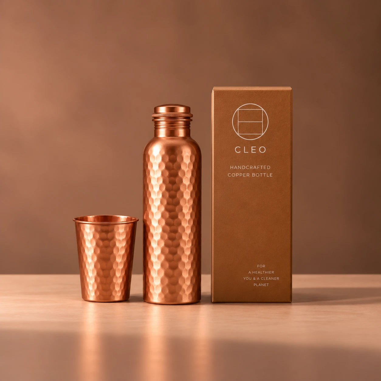 Hammered copper bottle and matching tumbler beside the kraft box
